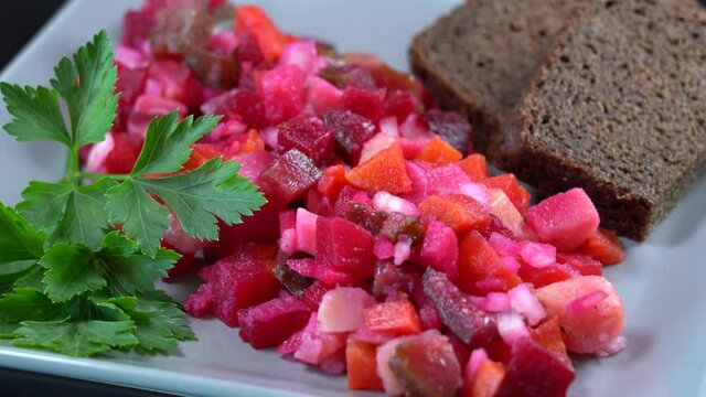 Ukrainian salad vinaigrette, salad from boiled vegetables, beetroot, carrot, potatoes mixed with pickled cucumber and dressed with vinegar or oil, served in restaurant, rotates in black background
