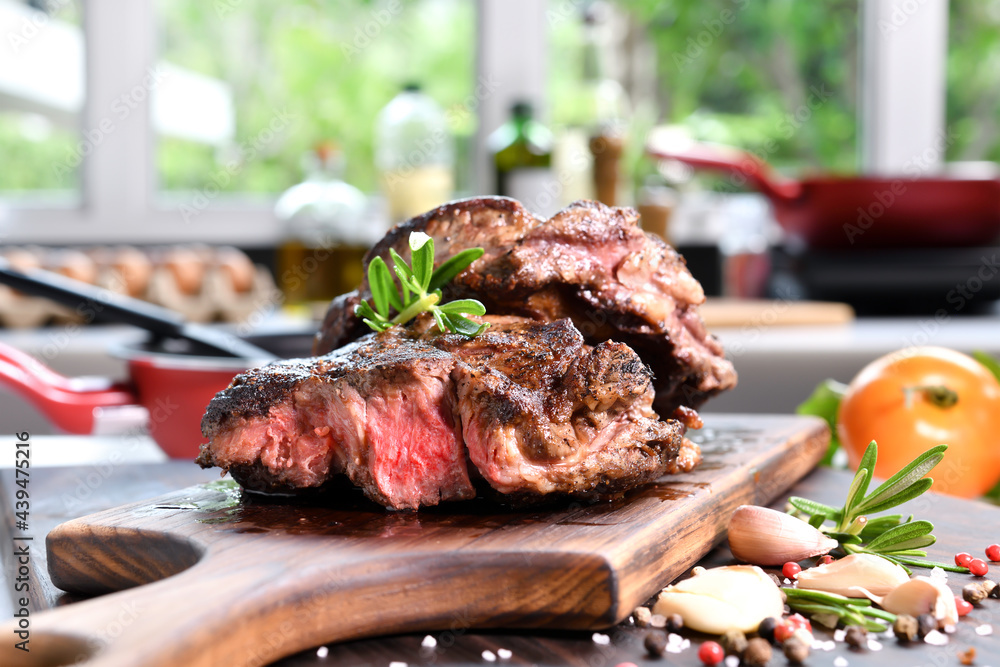 Wall mural Grilled beef steaks with spices on wooden cutting board in the kitchen