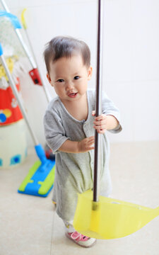 Cute Asian kid playing with broom on home balcony