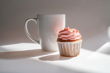 A cupcake or muffin stands next to a cup of coffee.