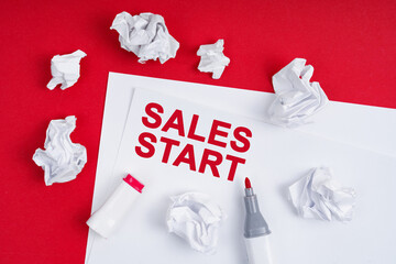 On a red background lies crumpled paper, a marker and a sheet of paper with the inscription - SALES START