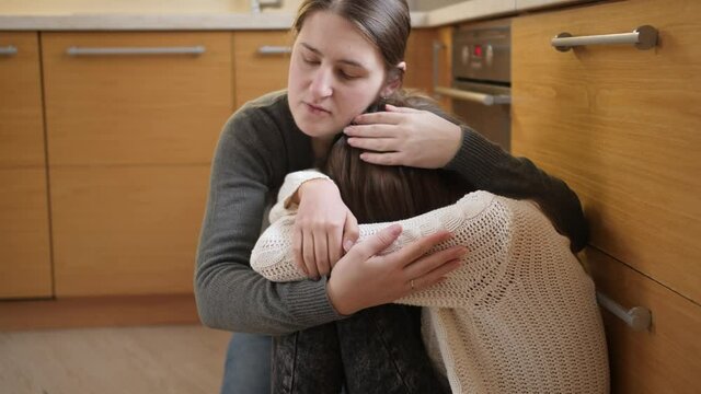 Young mother comforting and calming her daughter crying on floor at kitchen. Concept of domestic violence and family aggression and teenager depression.