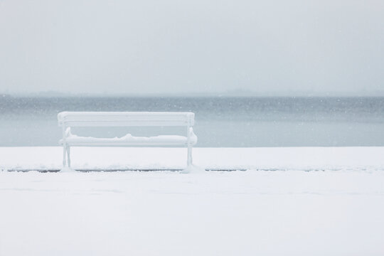 A bench by the lake covered in snow.