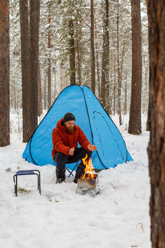 Male hiker sitting near fire in winter forest