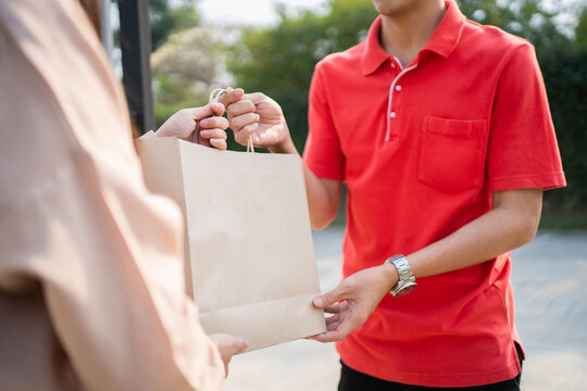 Young Asian woman receiving food and drink package from delivery service company staff at home