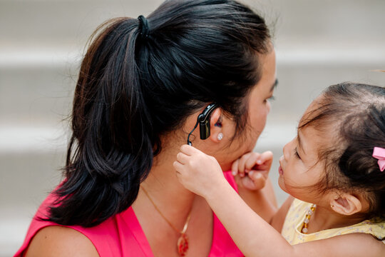 Curious young girl examines Asian mother's cochlear implant 