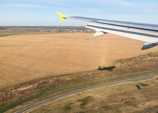 View Of Airplane Wing, Shadow Of The Plane On The Ground During Landing, Seen From The Plane Window.