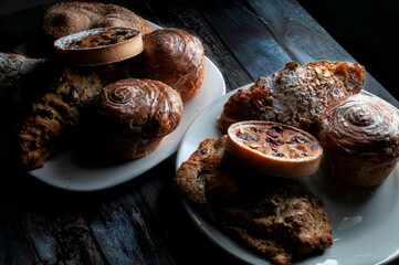 Angle view of sweet bread on white plates lit by a moody evening light from a window, low key light, dark food photography, baroque or renaissance style.