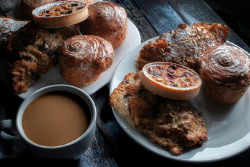 Horizontal sweet bread on a white plate lit by a window in a moody evening morning ambient  with a cup of coffee and cream dark food, low key light photography baroque renaissance style
