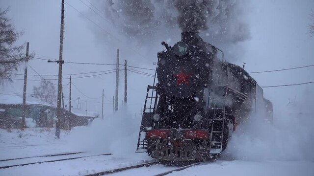Gimbal heavy snow blizzard old train steam locomotive rides in slow motion by rail railway railroad. Epic impressive steam engine wheel mechanism. Siberia Russia travel transsib. Beautiful snowfall