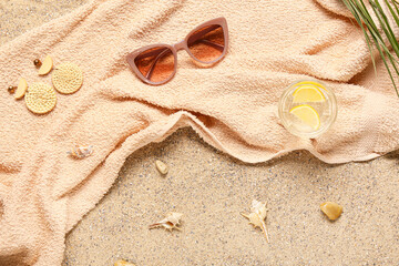Fototapeta na wymiar Stylish sunglasses with earrings, towel and glass of water on sand
