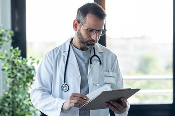 Concentrate handsome male doctor with eyeglasses reviewing medical reports in medical consultation.