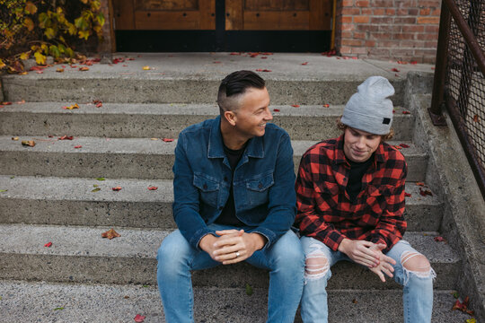 Father And Son Talking Together Outside On Steps In City Neighbo