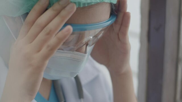 Asian doctor or nurse suffering from a headache and rubbing her temples while working in a hospital during coronavirus pandemic.