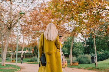 senior woman from back with yellow coat relaxing at park in autumn