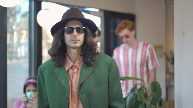 Three confident retro dandy men with vintage tape recorder on shoulder leaving vintage coffee shop. Young friends walking away with serious facial expression. 1980s lifestyle and friendship