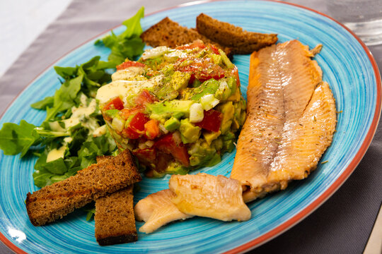 Image of tasty salad guacamole with arugula and tomatoes aerved with grilled trout fillet at plate