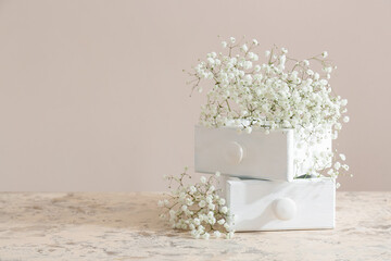 Beautiful gypsophila flowers and drawers on table near color wall