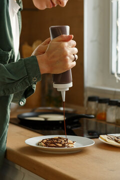 Crop female squeezing chocolate sauce on pancake