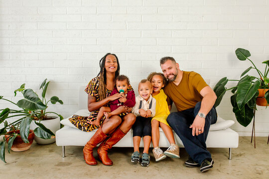 Happy biracial family seated on bench in front of white wall