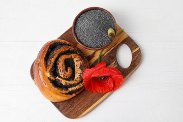 Bowl with poppy seeds, flower and tasty bun on light wooden background