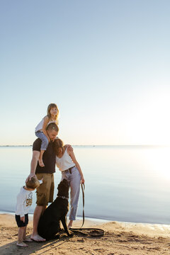 Idyllic family with dog cuddling on sandy seacoast during summer holidays