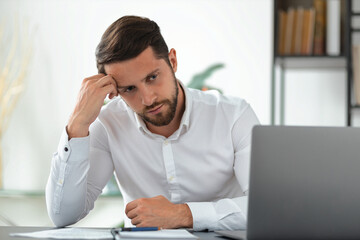 Frustrated businessman looking at laptop screen, analyzing bad sales month, sitting at work table in office, poor financial result of the month, bankrupt