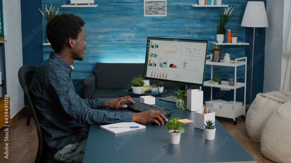 Poster african american guy working from home, taking notes on notepad while remote working on computer fro