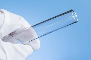 Medical laboratory. A gloved hand holds an empty test tube against a blue background.