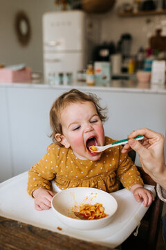 Baby girl with polkadot dress eating pasta in a high chair