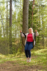Middle aged woman in the woods swinging on a swing made from an old car tire
