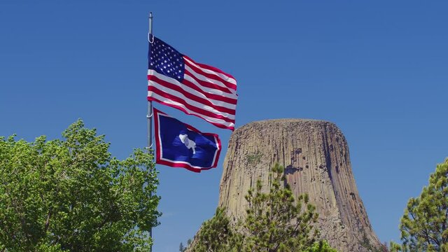 American Flag and Wyoming State Flag blowing in the wind viewing Devils Tower in the distance.