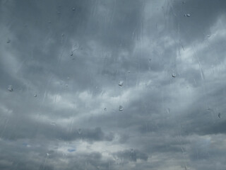 Window glass in a rainy day. Raindrops on window with cloudy sky background