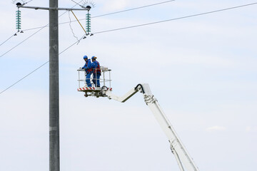 A team of electricians maintains the overhead power line. They look down from a height on the surrounding area. Copy space.