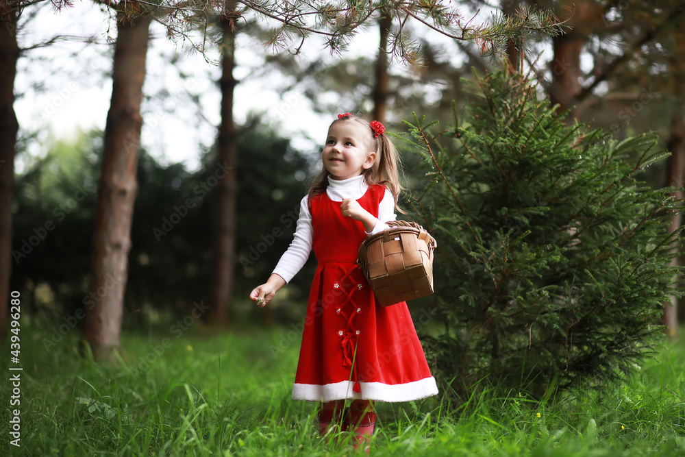 Wall mural A little girl in a red hat and dresses is walking in the park. Cosplay for the fairytale hero 