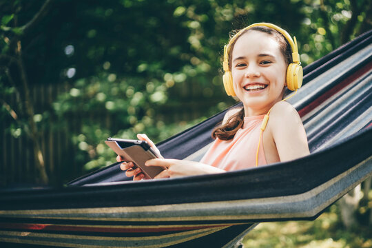 Young girl with smile using tablet on the hammock.