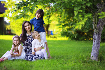 Obraz premium Young large family on a summer morning walk. Beautiful mother with children is playing in the park.