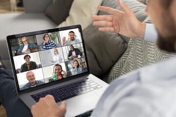 Young caucasian man using laptop for having virtual team meeting on video call with different...