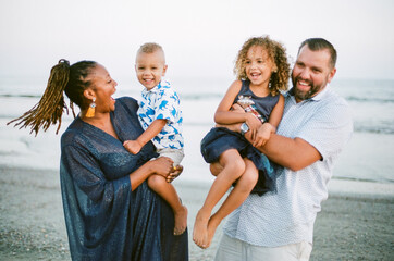 Laughing biracial family on beach at sunset