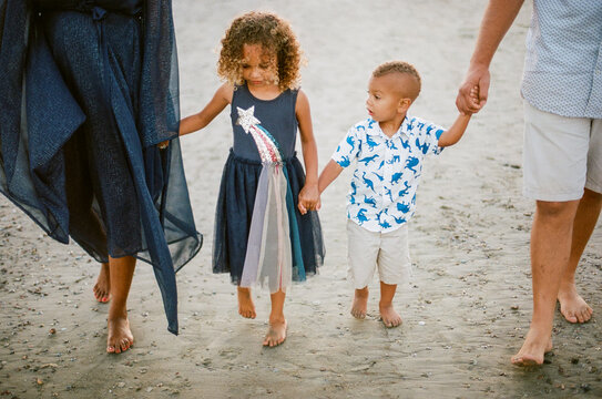 Biracial siblings walking on beach with parents