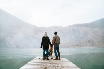 Couple on wooden dock in frozen lake in mountain with dog
