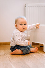Fototapeta premium Adorable baby sitting on the floor of the house and looking away