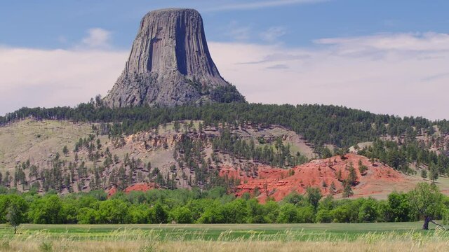 View of Devils Tower across field as grass blows in the wind in Wyoming as clouds move on the horizon.
