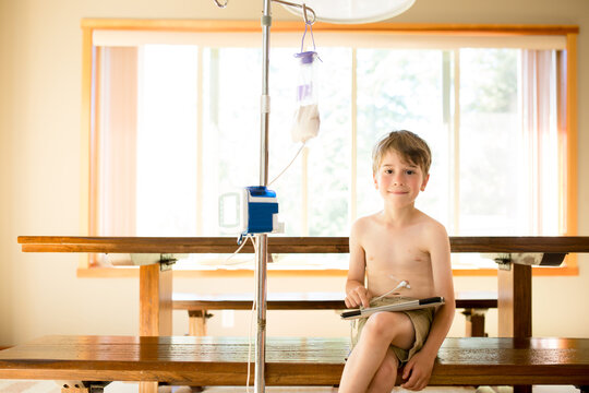 Smiling boy with g-tube holds  tablet while being fed