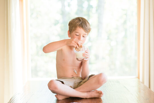 boy with g-tube sits on dining table dipping cookie into milk