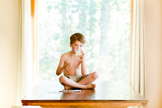 Boy with g-tube port sits on dining table drinking milk and eating cookie
