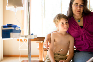 Boy being fed through g-tube smiles at viewer  while mother reads to him 