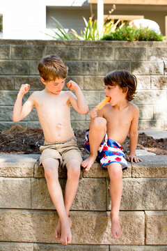 Young Boy flexes his muscles as friend with popsicle looks on