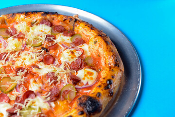 Pizza with bavarian sausages, Mozzarella cheese, onion and cucumbers isolated on blue background.
