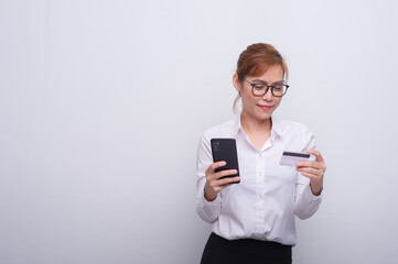 Portrait of smiling asian woman holding credit card and mobile phone isolated over white background